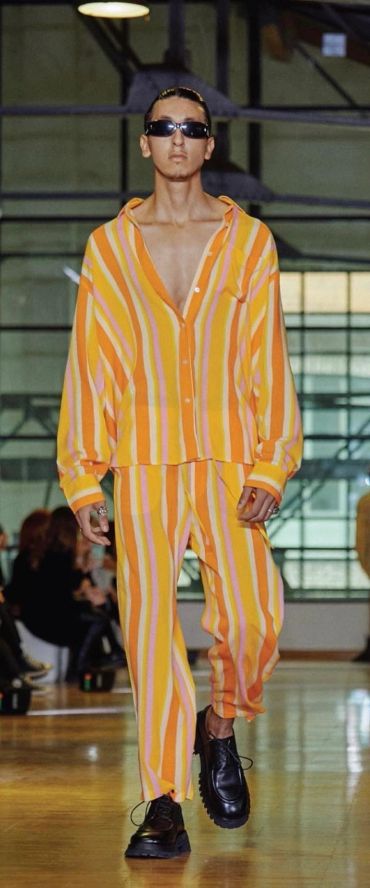 Model walking runway in yellow-orange striped outfit.