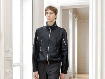 Young man in a black jacket standing indoors.