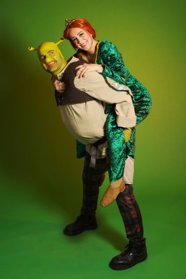 Two people dressed as Shrek and Fiona with a green background.