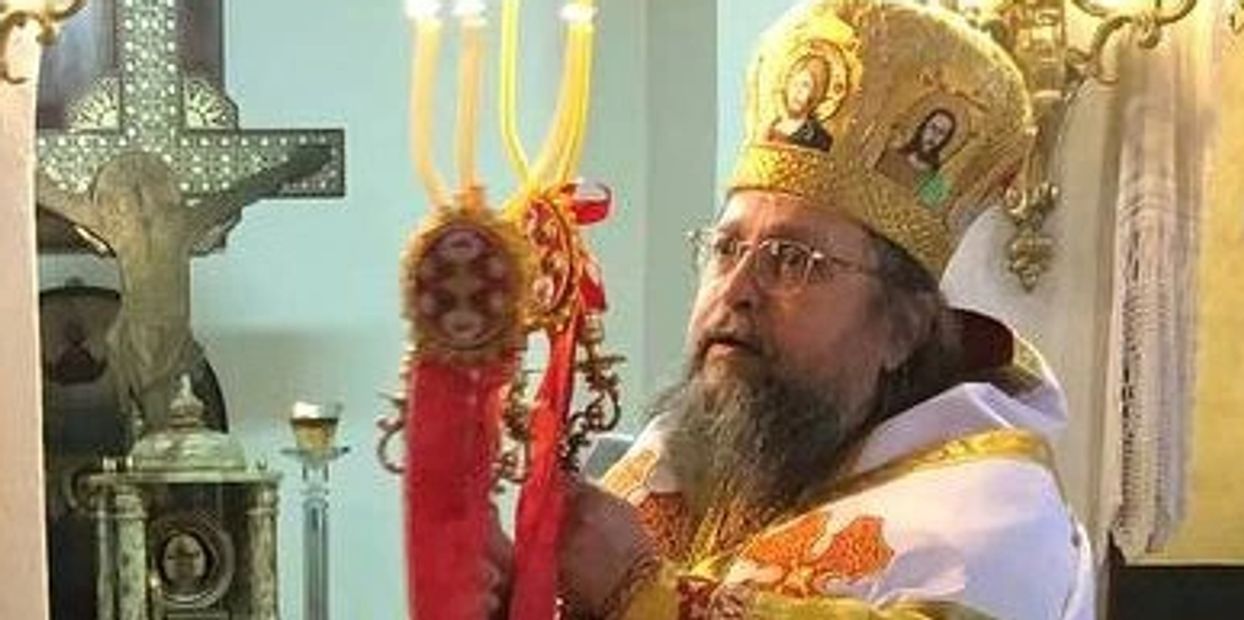 Orthodox priest holding ceremonial candle inside a church.