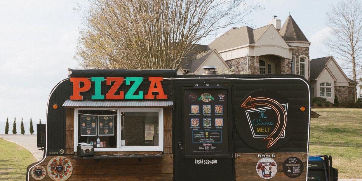A black pizza food truck with colorful signage and menu in a suburban setting.