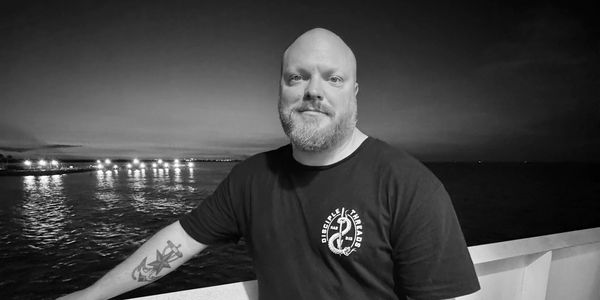 Man with tattoo on arm stands by water at night.