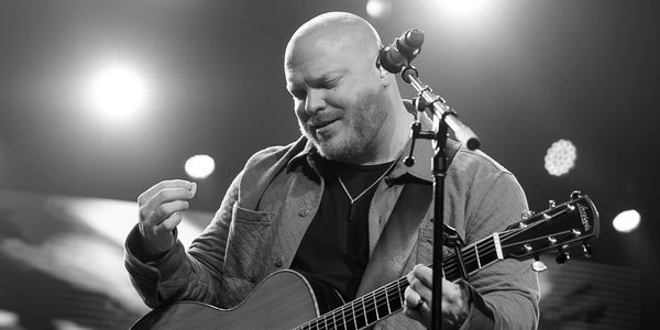 Musician playing guitar and singing on stage.