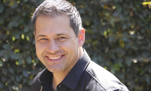 Man smiling outdoors with greenery background.