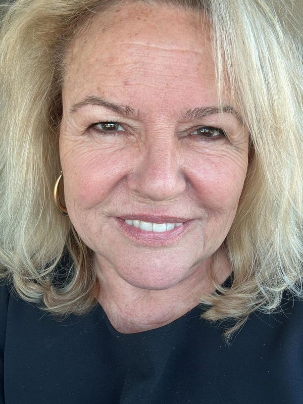 Smiling mature woman with blonde hair and gold hoop earrings.