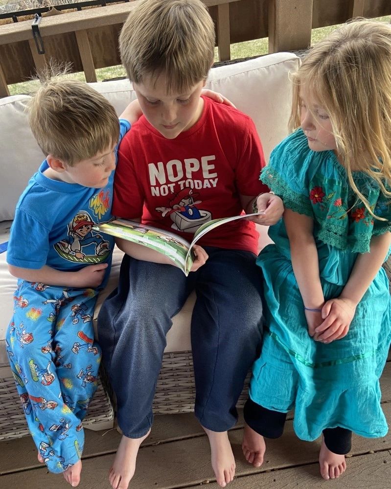 Cameron reading The Backyard to his younger siblings Olivia and Brooks.