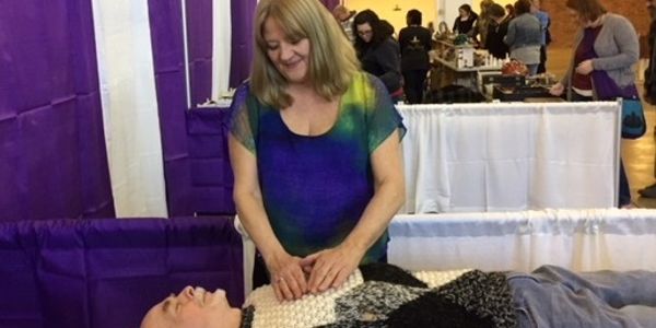 Woman giving a massage to a person lying down at an event.