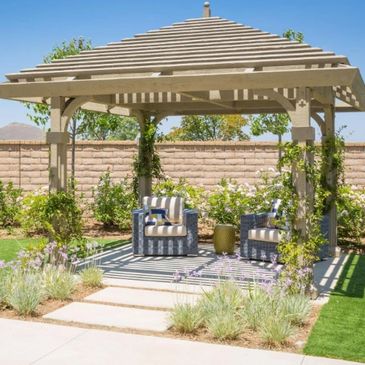 Cozy backyard pergola with two cushioned chairs and greenery.