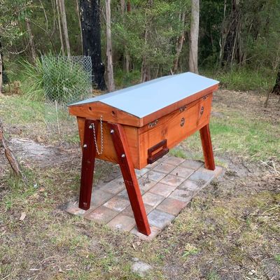 Wooden beehive stand with metal roof in a forest setting.