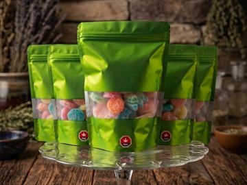 Green resealable bags filled with colorful gummy candies on a glass stand.