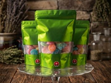 Green resealable bags with colorful gummies on a glass stand.