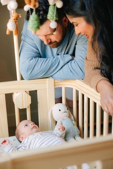 Parents lovingly watch their baby in a crib with a stuffed toy.