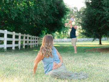 A woman sitting on grass watching a man lifting a child in a park.