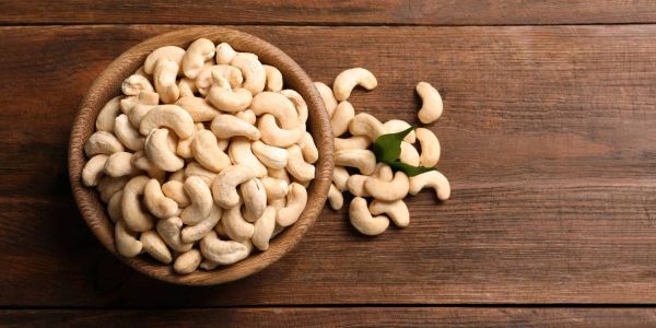 A bowl filled with raw cashew nuts on a wooden table.