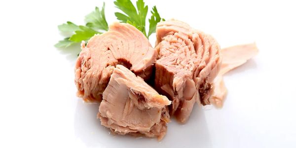 Chunks of cooked tuna garnished with parsley on white background.