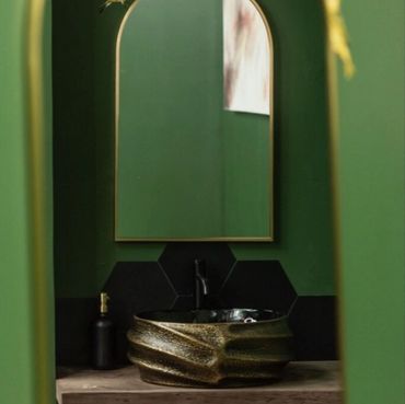Elegant bathroom with green walls and a unique gold sink under an arched mirror.