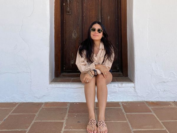 Woman sitting on a step in front of a wooden door with white walls.