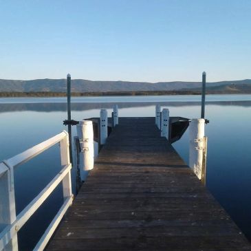 Wooden dock extending over calm water with hills in the background.