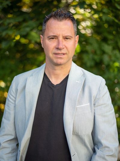 Man in a light gray blazer and black shirt outdoors.