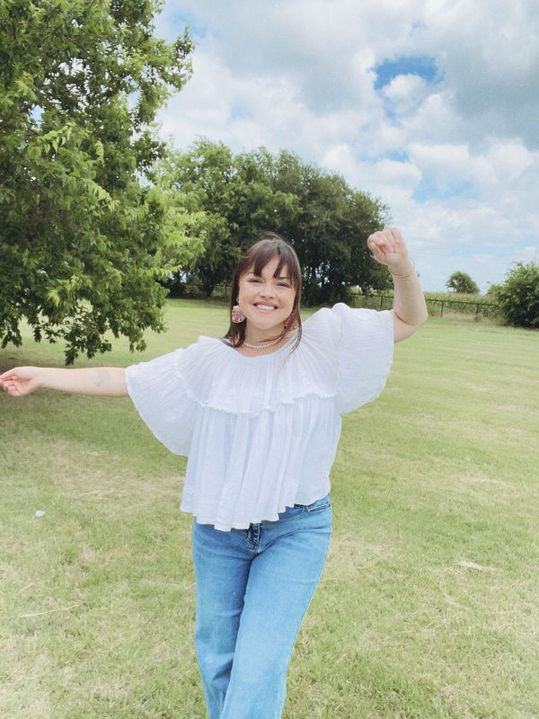 A woman joyfully posing outdoors in a white blouse and jeans.