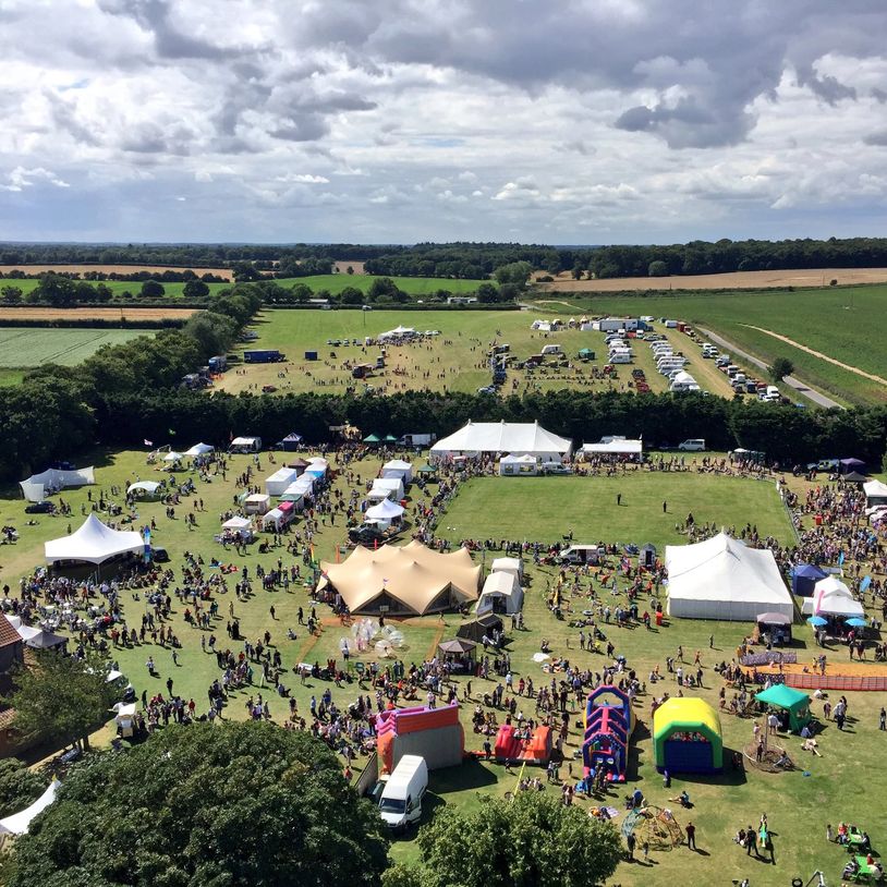 A drone shot of a packed event with a field filled with marquees and lots of people milling about.