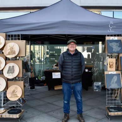 Mark stood outside his gazebo, smiling with racks of laser engraved pieces on display outside