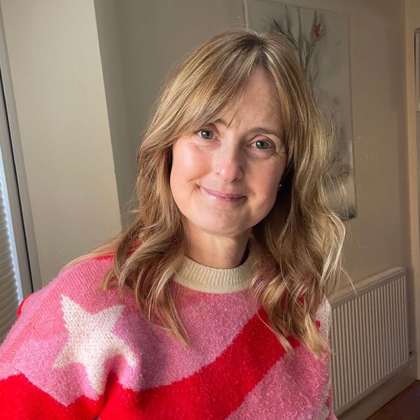 Smiling woman with wavy blonde hair wearing a colorful star-patterned sweater.