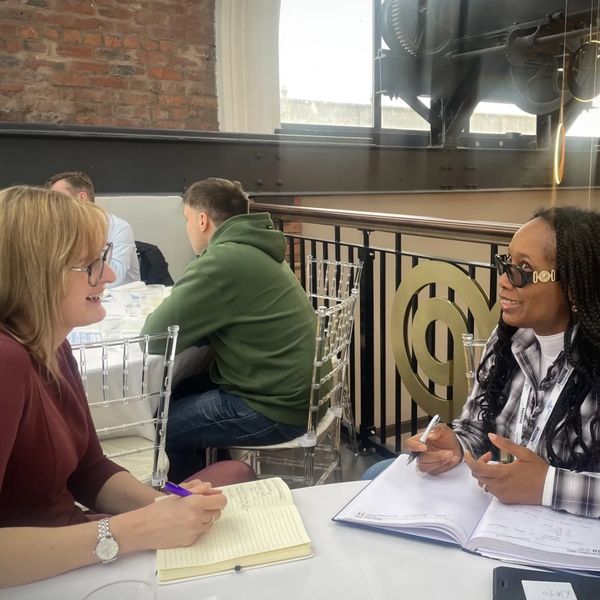Two women engaged in a friendly discussion with notebooks open.