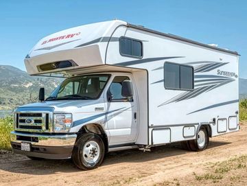 White Sunseeker RV parked on a dirt path with mountains in the background.