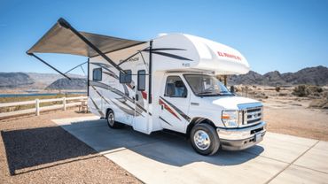 A white motorhome with an extended awning parked in a desert campsite.