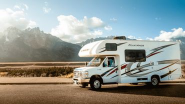 A white RV parked with mountains in the background under a blue sky.