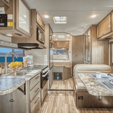 Interior view of a modern, stylish RV kitchen and dining area with wood finishes.