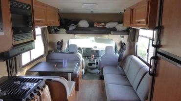 Interior view of a cozy RV with seating, a small dining area, and a sleeping loft.