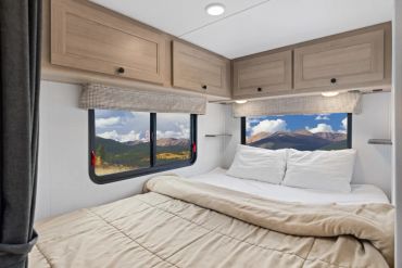 Cozy RV bedroom with mountain views through windows.