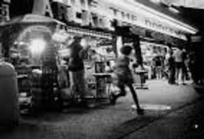 A child runs past a busy street scene at night with people outside a lit storefront.