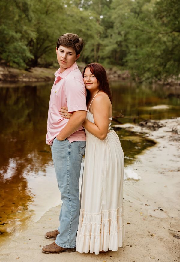 couple standing on the sandy bank of river hugging, smiling 