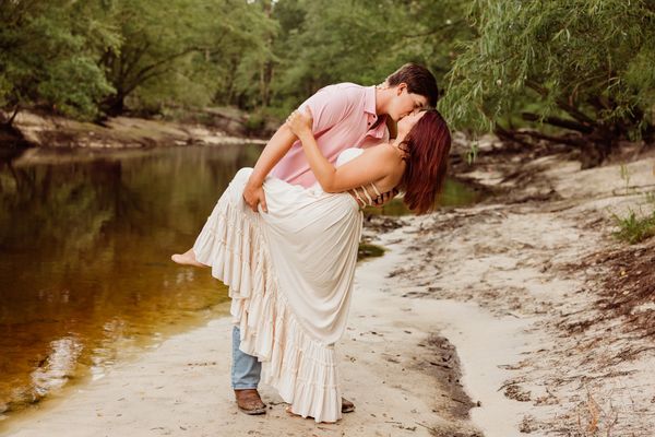 couple standing on sandy bank of river kissing