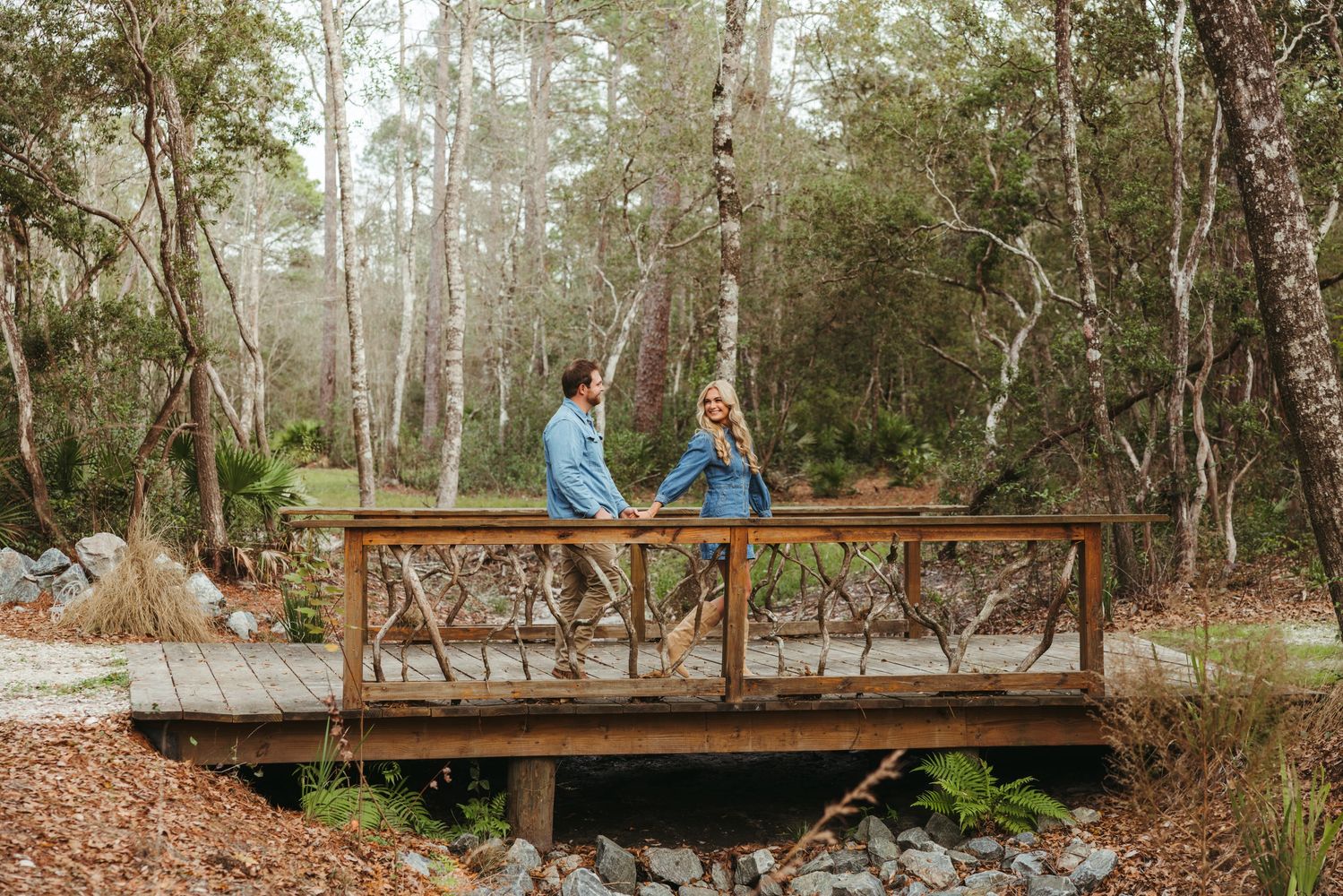 Couple holding hands on a rustic wooden bridge in a forest.