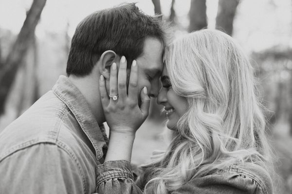 couple with foreheads touching, eyes closed but smiling, woman's hands on mans face showing off ring
