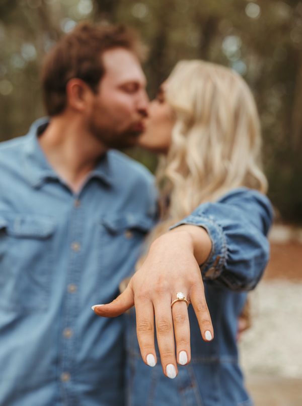 couple kissing, woman's hand is outstretched showing off engagement ring 