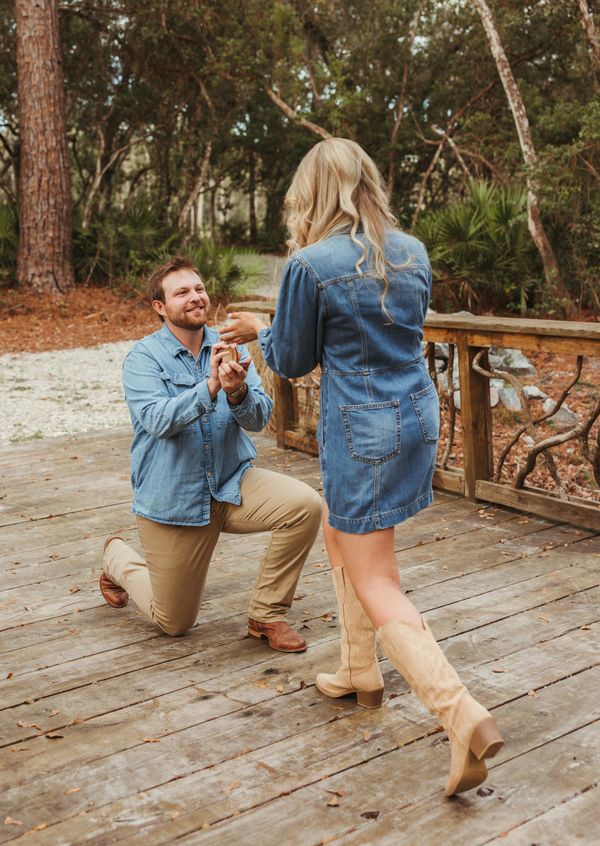 proposal, man is standing on wooden walking bride on one knee smiling at woman he is proposing to 