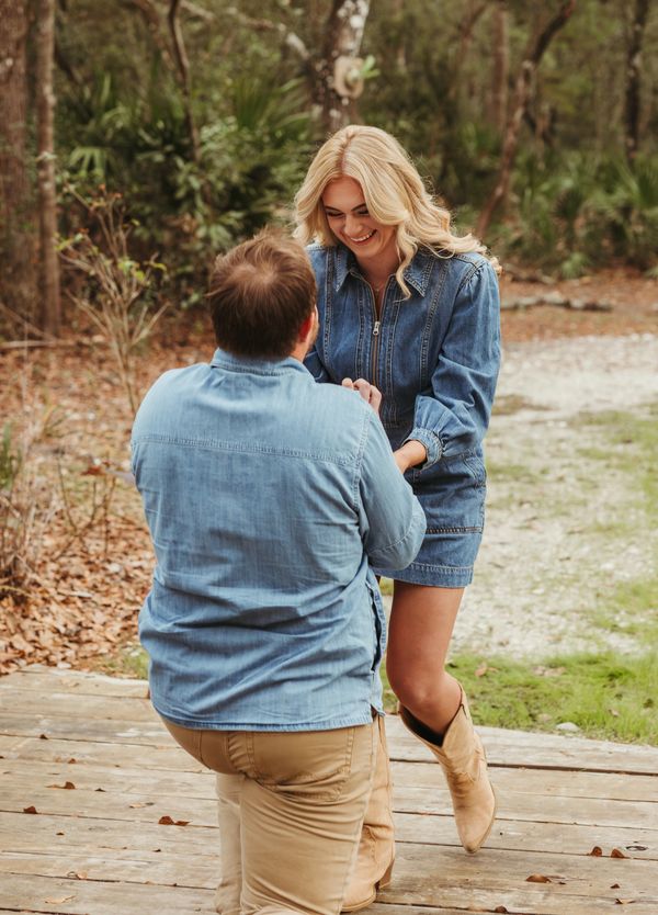 proposal, man is on one knee and woman is smiling joyfully looking at him 