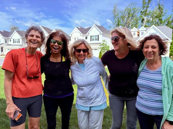 Five women smiling outdoors on a sunny day.