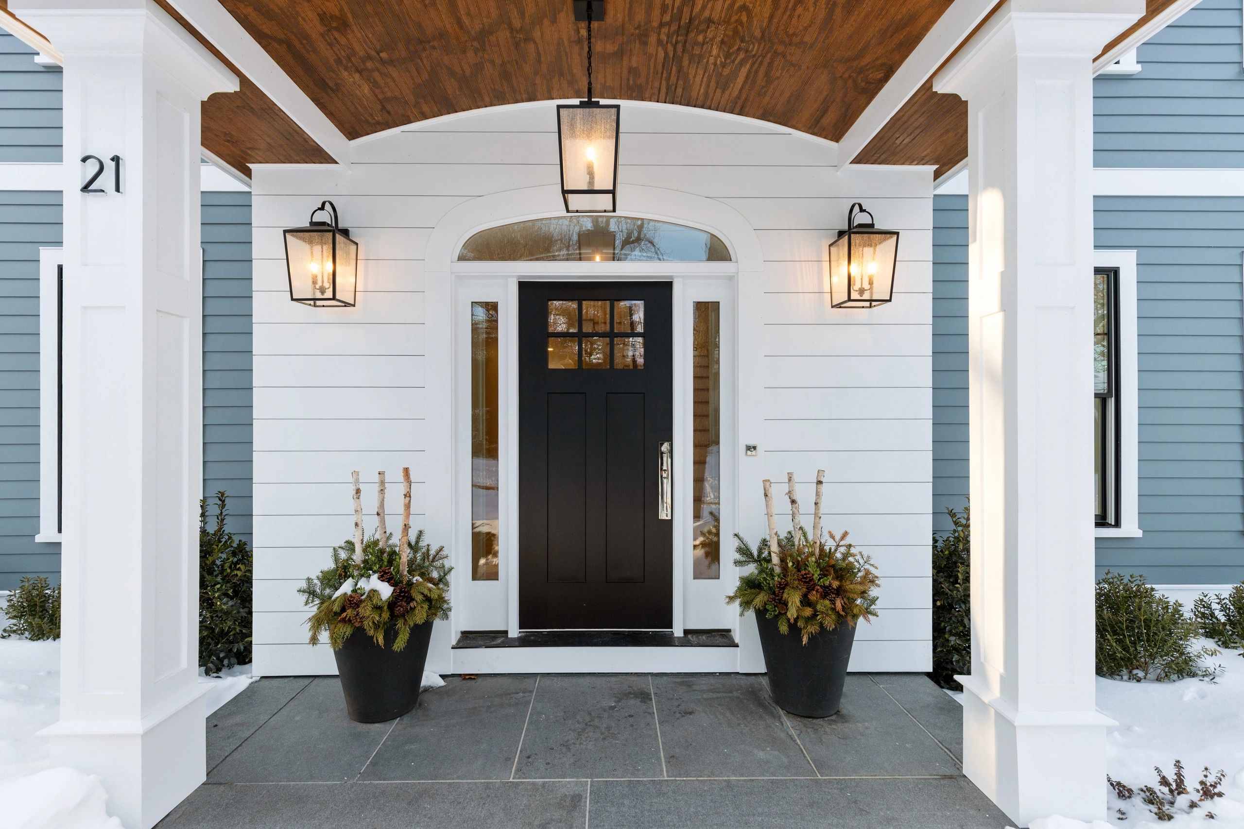 Elegant front porch with black door, white columns, and festive planters.