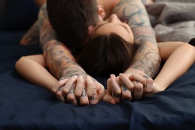 A couple lying closely, holding hands intimately on a dark bed.