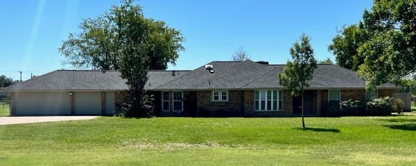 Single-story brick house with a large green lawn and clear blue sky.