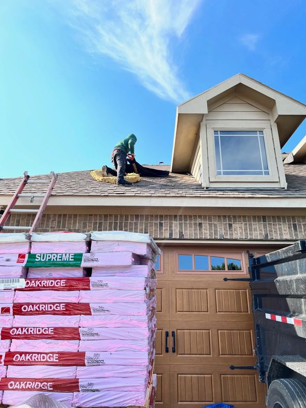 Worker installing roofing materials on a house roof under clear blue sky.