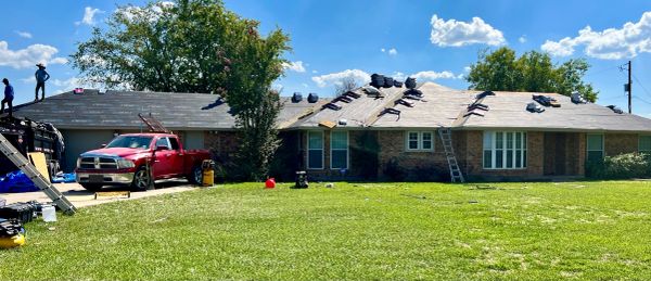 Workers repairing the roof of a single-story house on a sunny day.