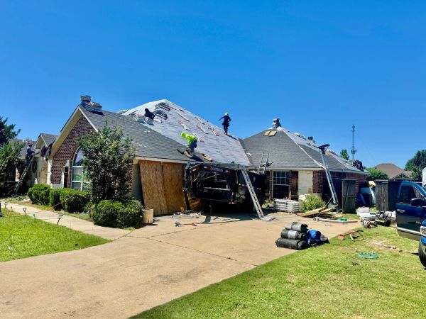 Workers replacing the roof of a suburban house on a sunny day.