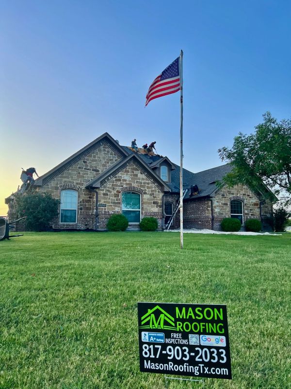 Roofers working on a house with an American flag and Mason Roofing sign in front.
